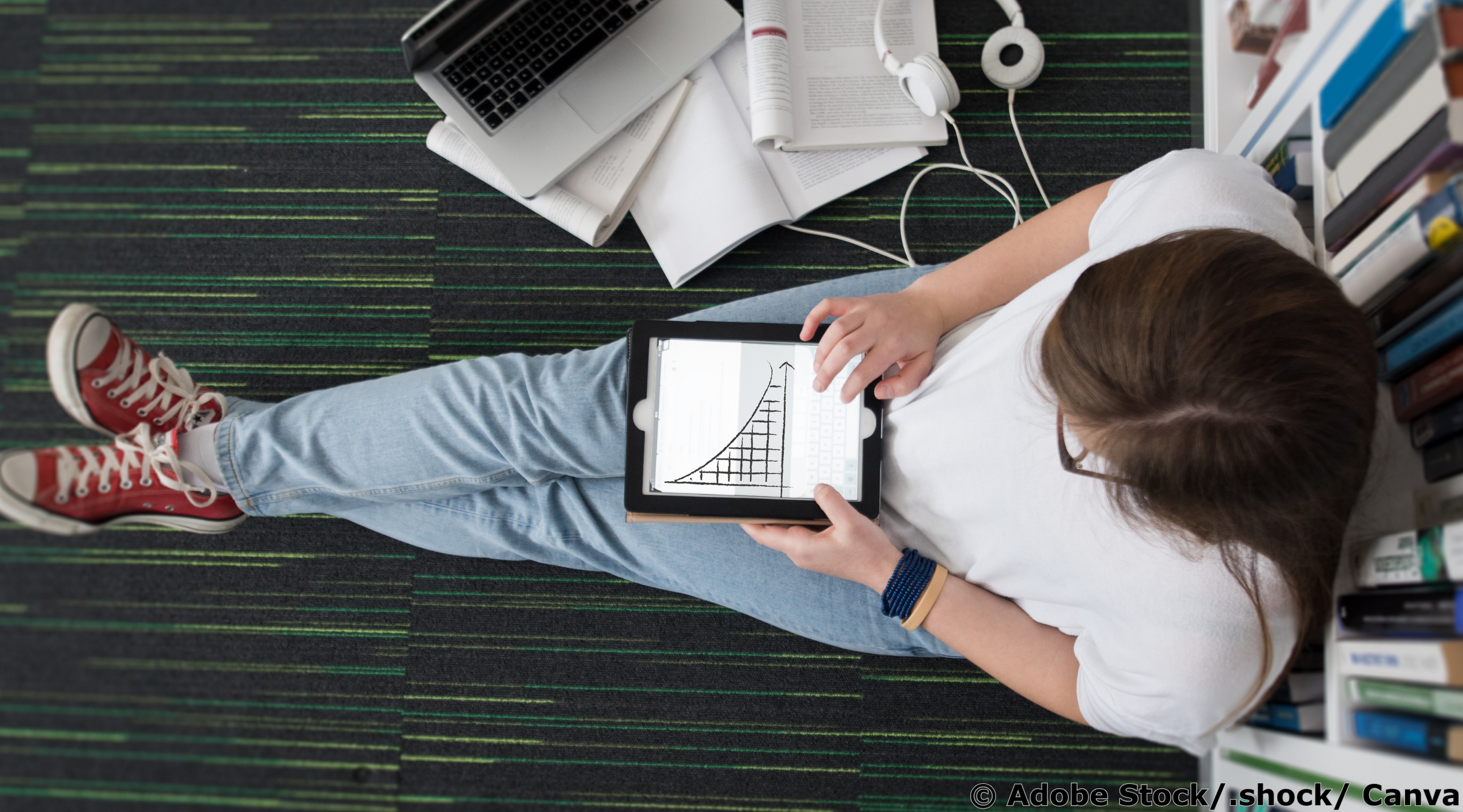 Junge Frau sitzt auf dem Boden einer Bibliothek und arbeitet mit einem Tablet, auf dem eine sinkende Exponentialfunktion zu sehen ist.