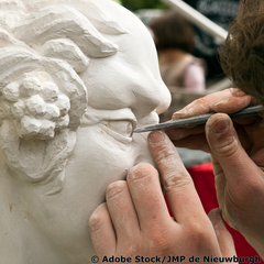 Bildhauer arbeitet mit einem feinen Instrument an dem Auge einer Skulptur. 