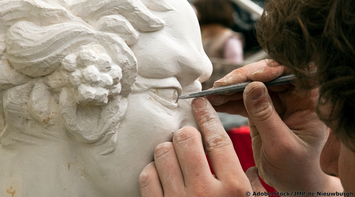 Bildhauer arbeitet mit einem feinen Instrument an dem Auge einer Skulptur. 