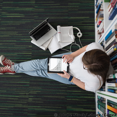 Junge Frau sitzt auf dem Boden einer Bibliothek und arbeitet mit einem Tablet, auf dem eine sinkende Exponentialfunktion zu sehen ist.