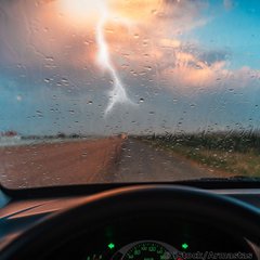 Ein blauer Himmel mit dunkler Wolke und Blitz ist zu sehen aus der Persepktive einer/s Autofahrer/in.