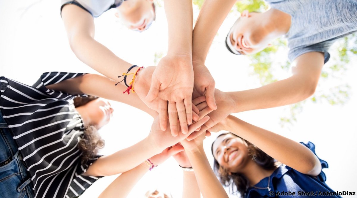 Das Bild zeigt eine Gruppe junger Menschen, die im Kreis stehen und ihre Hände in der Mitte übereinander legen, aufgenommen aus der Perspektive von unten nach oben.