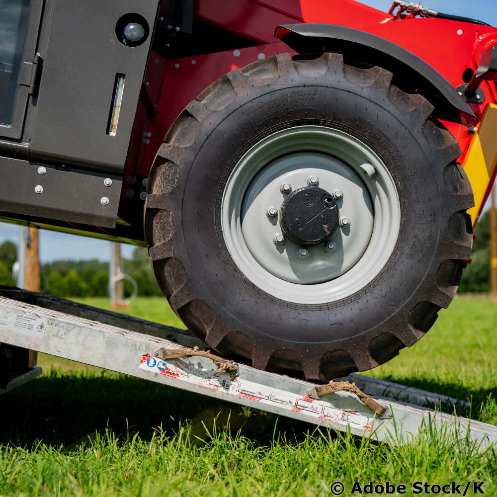 Ein roter Traktor wird über eine Metallrampe auf einen Anhänger verladen