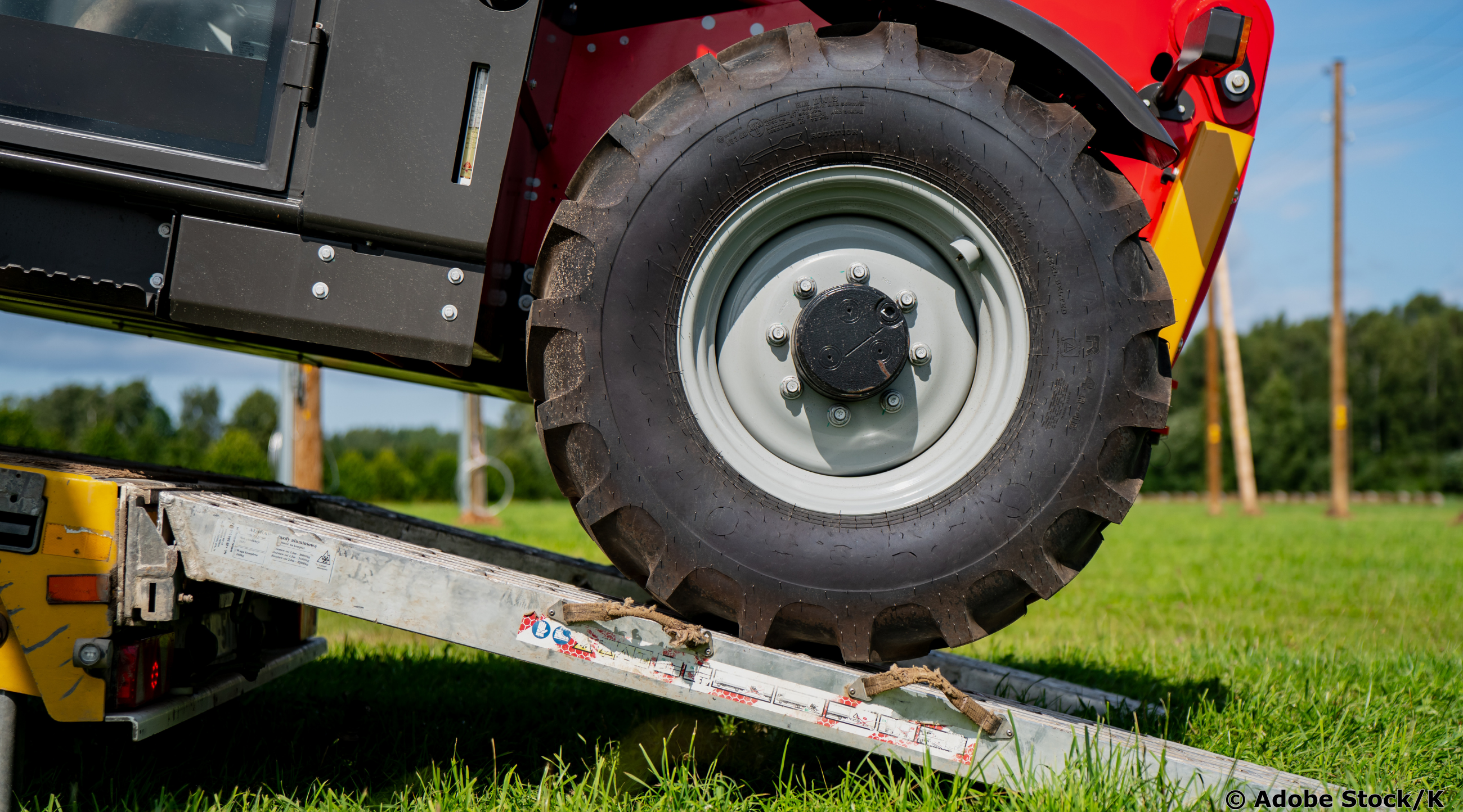 Ein roter Traktor wird über eine Metallrampe auf einen Anhänger verladen