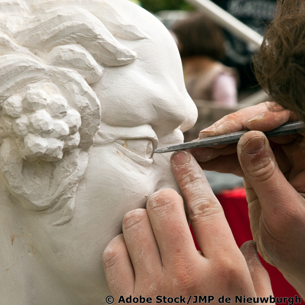 Bildhauer arbeitet mit einem feinen Instrument an dem Auge einer Skulptur.