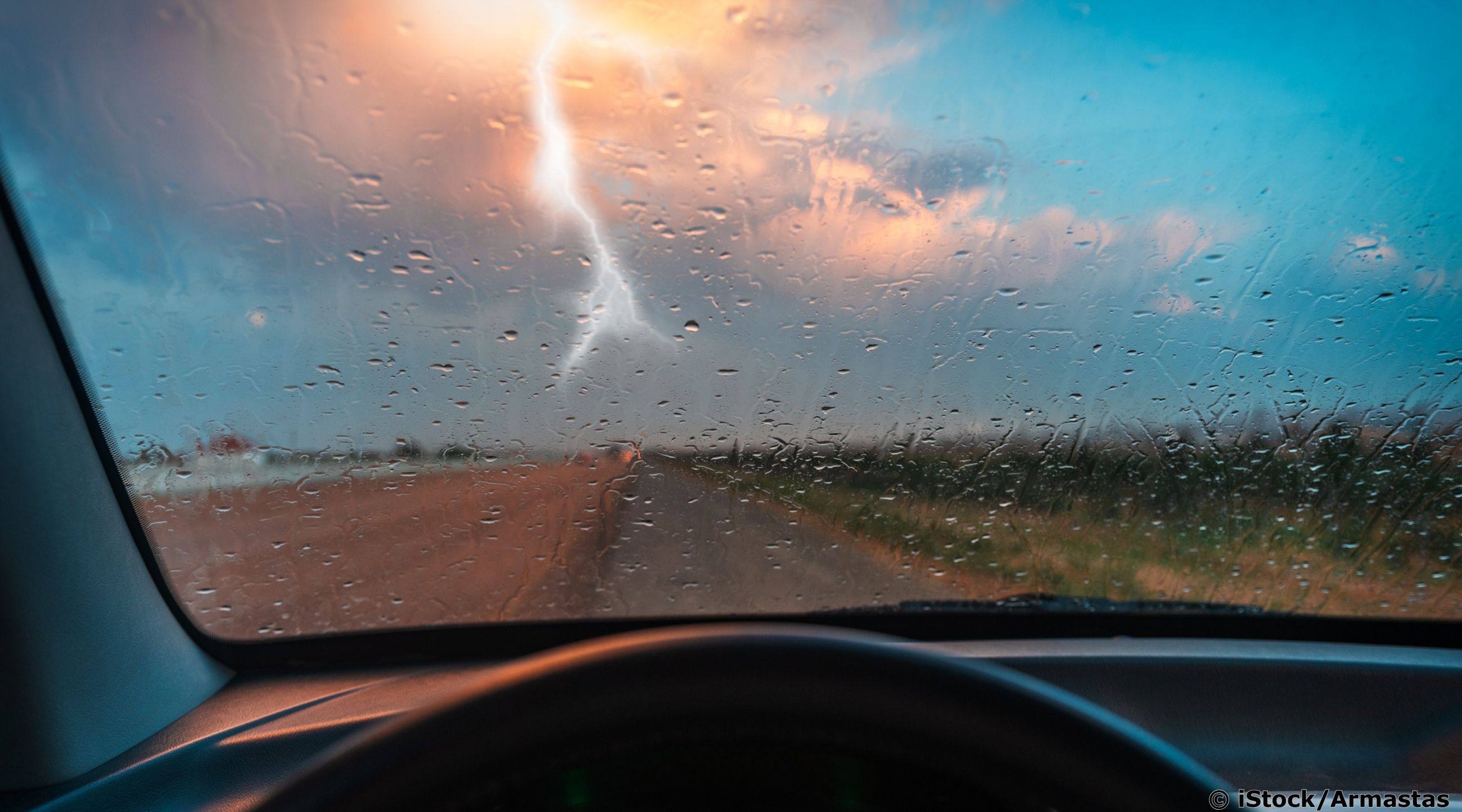 Ein blauer Himmel mit dunkler Wolke und Blitz ist zu sehen aus der Persepktive einer/s Autofahrer/in.