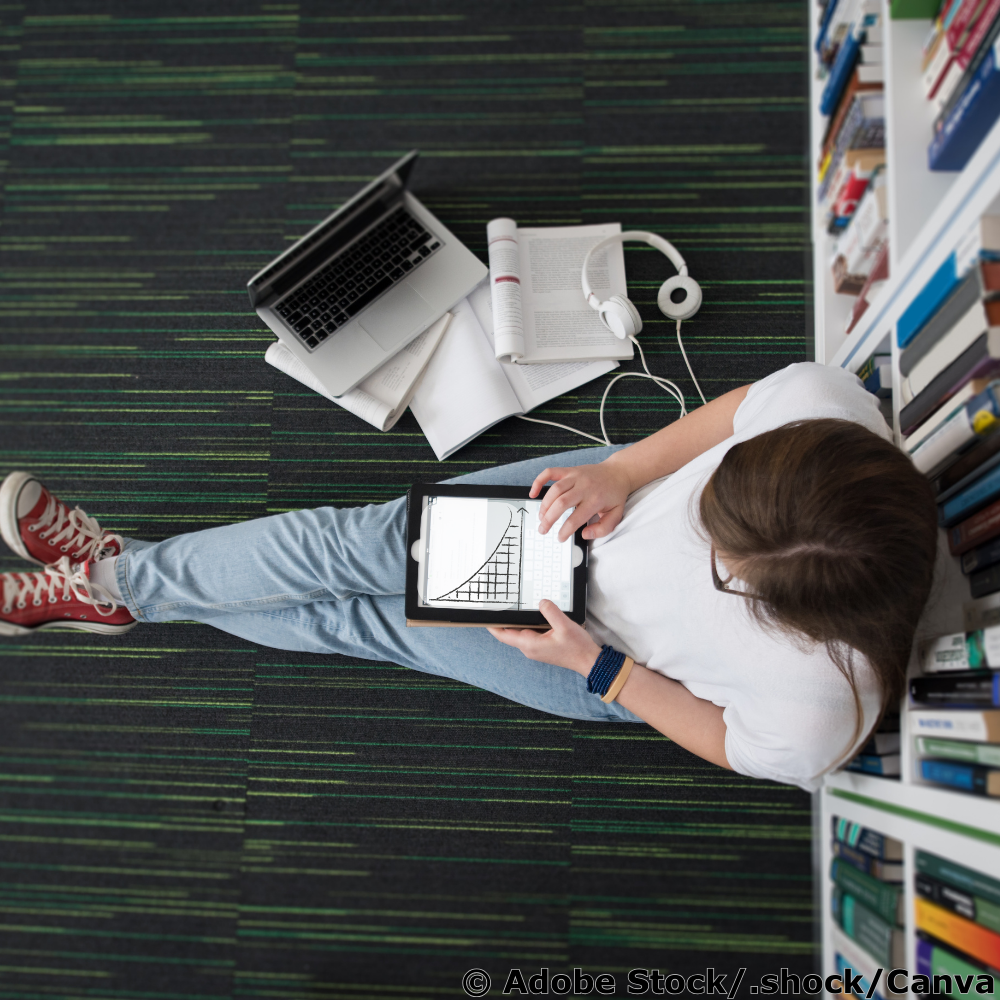 Junge Frau sitzt auf dem Boden einer Bibliothek und arbeitet mit einem Tablet, auf dem eine sinkende Exponentialfunktion zu sehen ist.