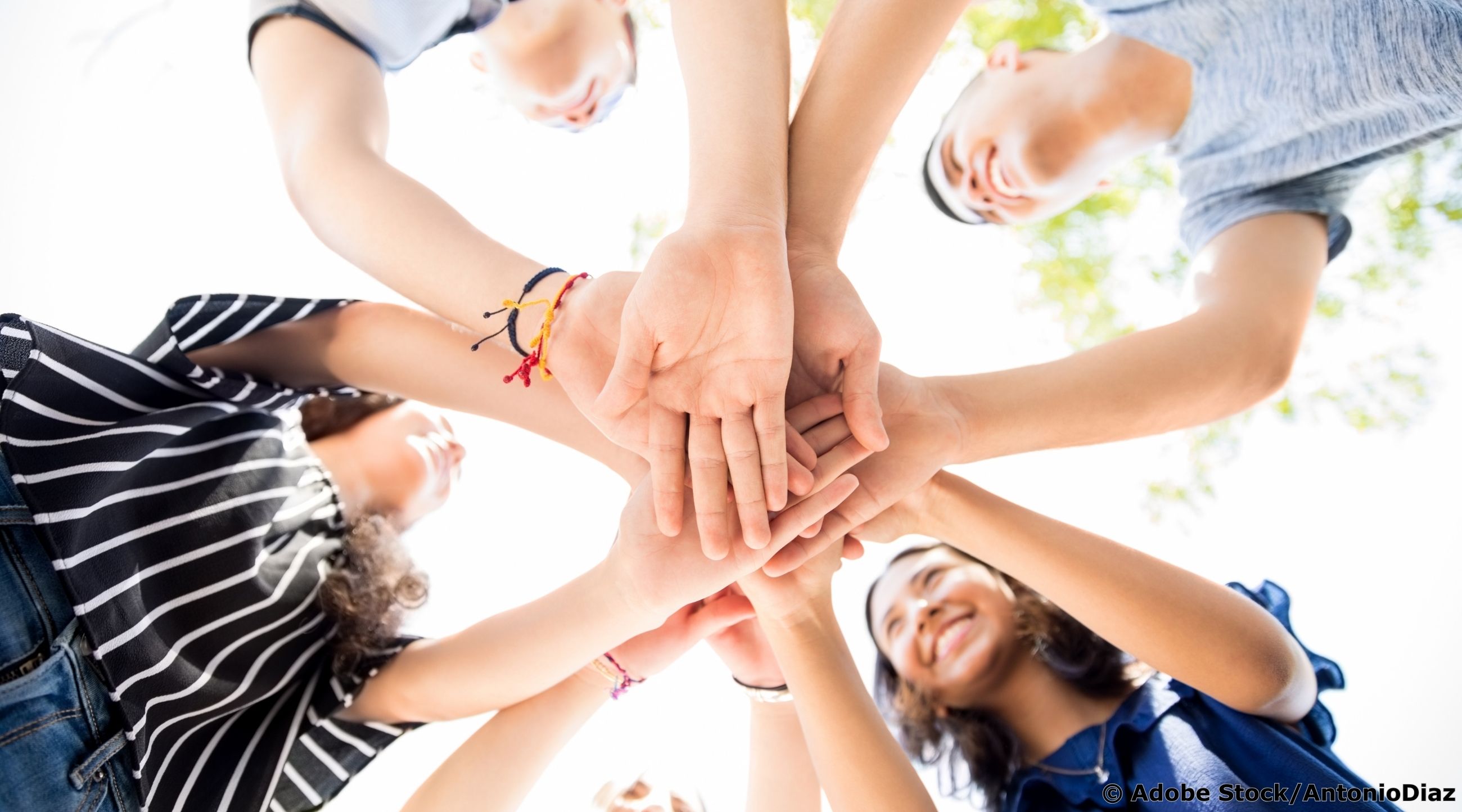 Das Bild zeigt eine Gruppe junger Menschen, die im Kreis stehen und ihre Hände in der Mitte übereinander legen, aufgenommen aus der Perspektive von unten nach oben.